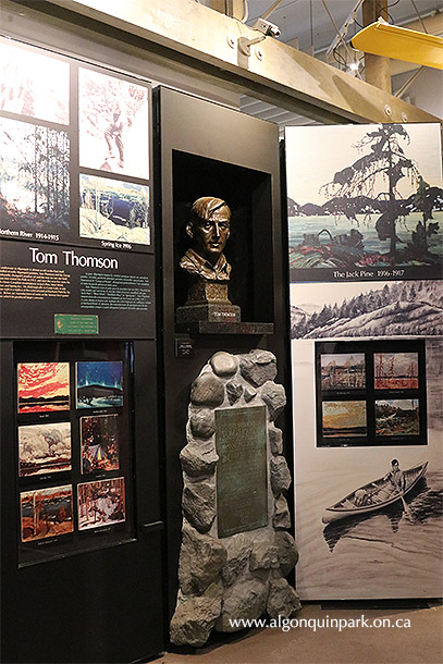 Image: A display in the cultural history exhibits at the Algonquin Visitor Centre highlights the life and works of Tom Thomson. A bust of the artist, sculpted by Sandra J. Shaw, sits above a replica of the stone cairn which is located on Canoe Lake.
