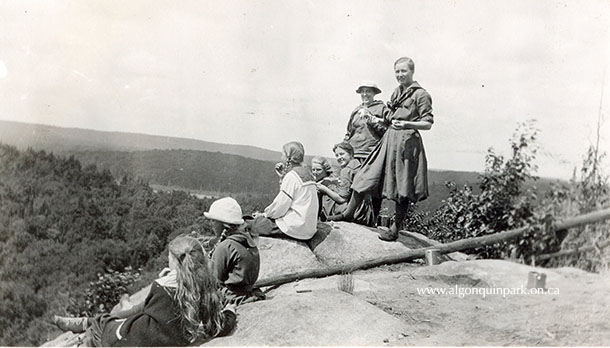 Image: Camp Northway campers at the top of Skymount overlooking Cache Lake, 1918. Early visitors to Cache Lake would climb the hill from the shore of Cache Lake to the rocky outcrop where the fire tower once stood. Later, one could follow the route along the railroad tracks from Algonquin Park Station. Today, Algonquin Park visitors reach the same lookout but by a different route, that of the Track and Tower Trail. APPAC, 2001.7.37. 
